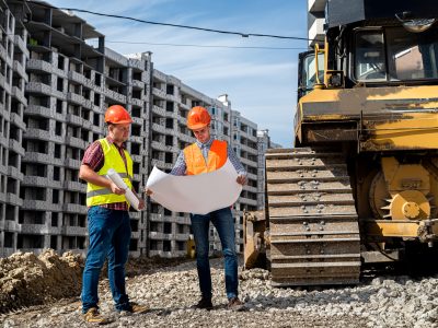 two young strong workers in uniform and helmets stand near a grader on a construction site. Construction concept